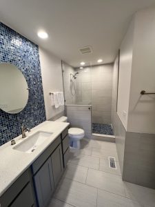 Bathroom with blue tile on wall. There is a glass shower.