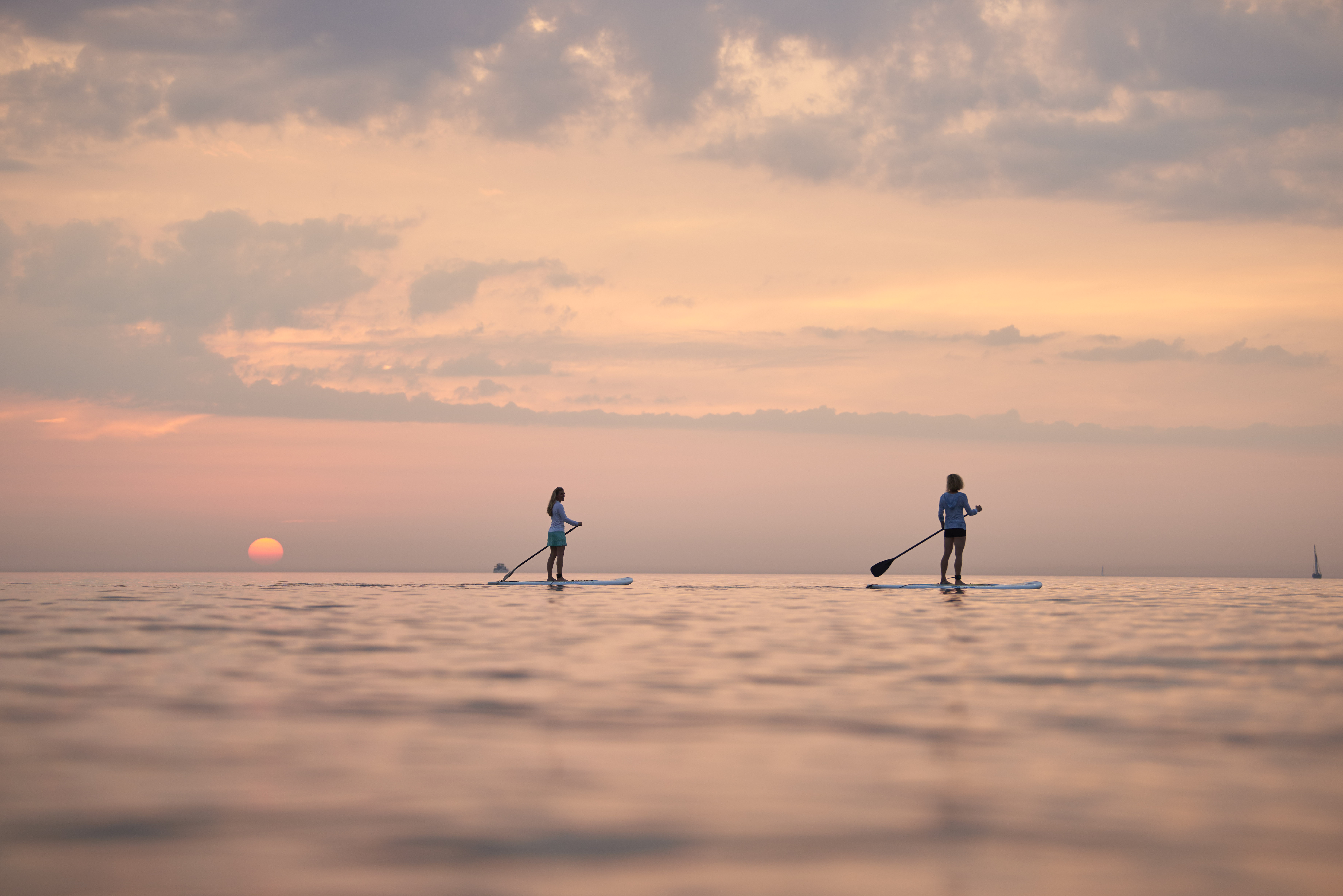 Two women paddleboarding on Lake Michigan during sunset.