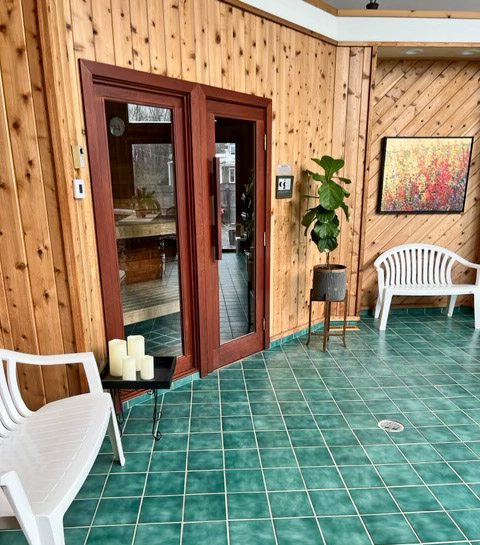 Sauna. Cedar plank wall. Tall plant against wall. Green tile on floor.